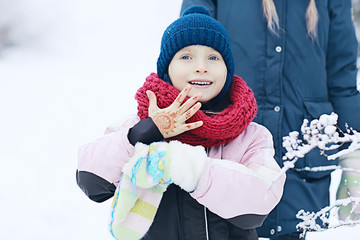 Wall Mural - child  playing in the snow / the girl in warm sports clothes is playing with snow on a winter walk. Warm woolen hat, down jacket. Concept of a happy baby walk.