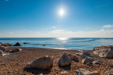 Wall Mural - Sandy beach, large stones, blue sea and bright sun - beautiful seascape