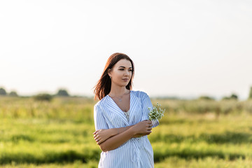 Wall Mural - attractive young woman with field flowers bouquet on green field under sunset rays