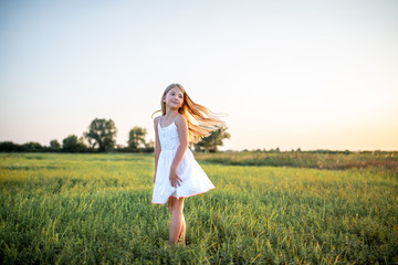 Wall Mural - adorable little child in white dress posing on field on sunset