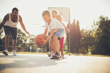 Wall Mural - Happy young parents with kids playing basketball.