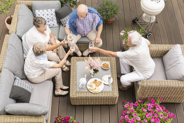 Top view of a wooden porch with happy senior men and women making a toast on the last day of their summer vacation in a luxury hotel.