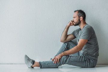 side view of frustrated bearded middle aged man sitting on floor and looking away