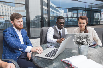 Wall Mural - Group of happy diverse male and female business people team in formal gathered around laptop computer in bright office against the background of a glass building