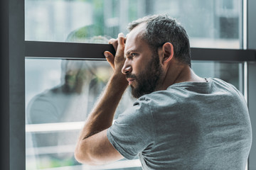 Wall Mural - upset bearded man leaning at window and looking through it