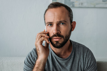 Wall Mural - frustrated bearded man talking by smartphone and looking at camera