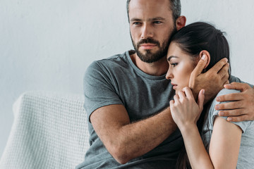 Wall Mural - bearded man supporting and hugging depressed woman sitting on couch