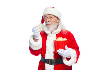 Christmas. Smiling, kind Santa Claus in white gloves with his mouth open holds a red bucket with popcorn with one hand, takes some popcorn and prepares to eat it with the second hand. The concept of