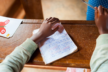 close up of little hand of african child at school with pen writing and learning on desk