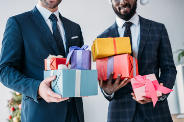 cropped image of smiling multicultural businessmen holding gift boxes in office