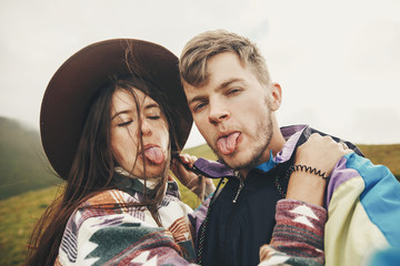 Wall Mural - happy hipster couple making selfie and showing colored tongues from blueberries on top of sunny mountains. family having fun and smiling. summer vacation. space for text.