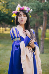 Medieval girl in a beautiful blue dress. A woman with long hair and a wreath of flowers. The model sits on a green lawn. Fantasy. Pinceess from the fairy tale.