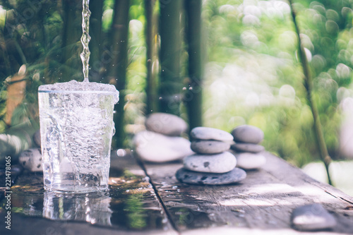 Cuadros en Lienzo Clean water pouring into the glass next to the stones on the old wooden table