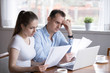 © fizkes - Serious husband and wife reading paper documents analyzing house utility bills, stressed couple get bank notice considering contract terms and conditions, man and woman managing paperwork and finances