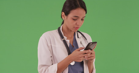Hispanic woman medical professional texting on mobile cell phone on green screen