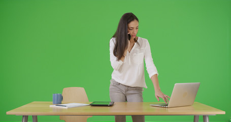 Hispanic businesswoman talking on phone and using laptop on green screen