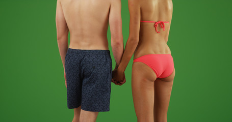 Wall Mural - Rear view of interracial couple in swimwear holding hands on green screen