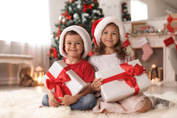 Canvas Print - Cute little children in Santa hats with Christmas gift boxes at home