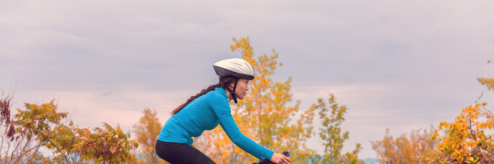 Wall Mural - Biking in fall autumn nature Asian cyclist girl riding bicycle doing outdoor sport in cold weather. Panoramic banner.