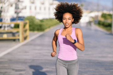 Black woman, afro hairstyle, running outdoors in urban road.