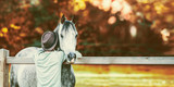 Fototapeta Konie - Guy bumped his head in neck of horse at fence in stable on background of autumn foliage