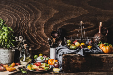 Various colorful tomatoes from garden, salad in plate, olives oil , mozzarella and kitchen tools on dark rustic table, front view. Still life