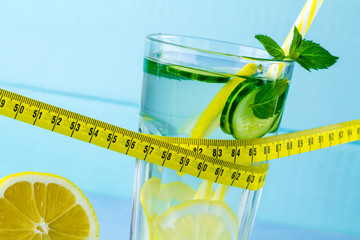 Wall Mural - Diet concept. Detox drinks. Lemon water in a glass, juicy lemon, mint and measuring tape on a blue background. Detox