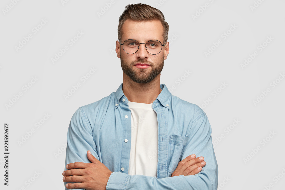 Horizontal shot of handsome self confident businessman or designer, stands crossed hands against white background, wears casual shirt, poses against white background. People and lifestyle concept - obrazy, fototapety, plakaty 