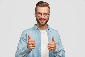 handsome young caucasian bearded man does okay symbol, keeps thumb raised, approves good idea of com