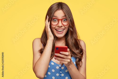Fotografie, Obraz Cheerful positive woman holds modern cell phone, forgets telephone number of boy