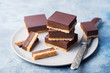 Chocolate caramel slices, bars, millionaires shortbread on a grey plate. Blue background. Close up.