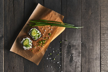 2 sandwiches with soft cheese, fresh cucumbers and green onions on rough wooden table