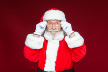 Christmas. Serious Santa Claus In White Gloves Adjusts Her Glasses And Stares Into The Camera. Isolated On Red Background.