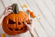 Woman Carving Big Orange Pumpkin Into Jack-o-lantern For Halloween Holiday Decoration On White Wooden Planks, Close Up View