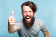 thumb up. good job. like and approval concept. enthusiastic motivated overexcited bearded man showing gesture. cas al hipster guy portrait on blue background.
