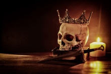 Human Skull, Old Book, Sword, Crown And Burning Candle Over Old Wooden Table And Dark Background.