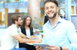 © ty - Young man holding digital tablet while his colleagues working in the background.