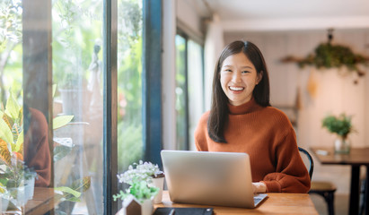 Happy young Asian girl working at a coffee shop with a laptop