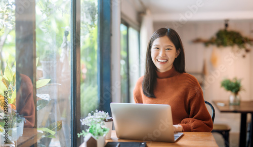 Zdjęcie: Happy young Asian girl working at a coffee shop with a laptop Happy young Asian girl working at a coffee shop with a laptop