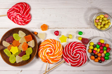 Colorful chocolate candies, lollipops and jelly sweets on white wooden table