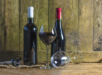 Two bottles of red wine and glasse of wine, corkscrew on rustic wooden background with copy space