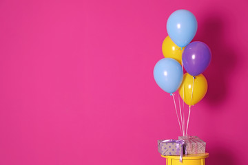 Bunch of bright balloons and gifts on table against color wall, space for text