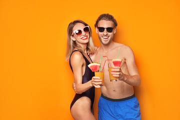 Canvas Print - Happy young couple in beachwear with cocktails on color background