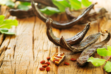 Sticker - Carob. Healthy organic sweet carob pods with seeds and leaves on a wooden table. Healthy eating, food background