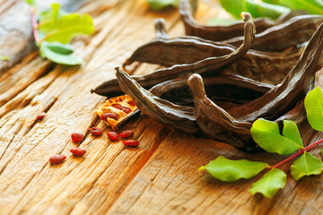 Sticker - Carob. Healthy organic sweet carob pods with seeds and leaves on a wooden table. Healthy eating, food background