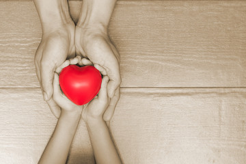 Hands of male dad and little child girl holding red heart ball together with blur green natural light bokeh background. Happy father's day father and daughter concept.