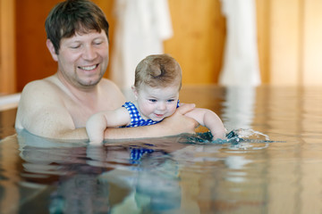 Wall Mural - Happy middle-aged father swimming with cute adorable baby daughter in whirl pool. Smiling dad and little child, girl of 6 months having fun together. Active family spending leisure in spa hotel