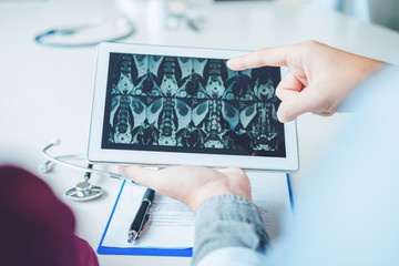 Doctor consulting with patient presenting x-ray film results on digital tablet tablet sitting at table