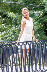 Young girl in white dress in summer park on the bridge
