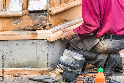 Fotografie, Tablou A male carpenter crouched down assembling a piece of wood on a house, outdoors
